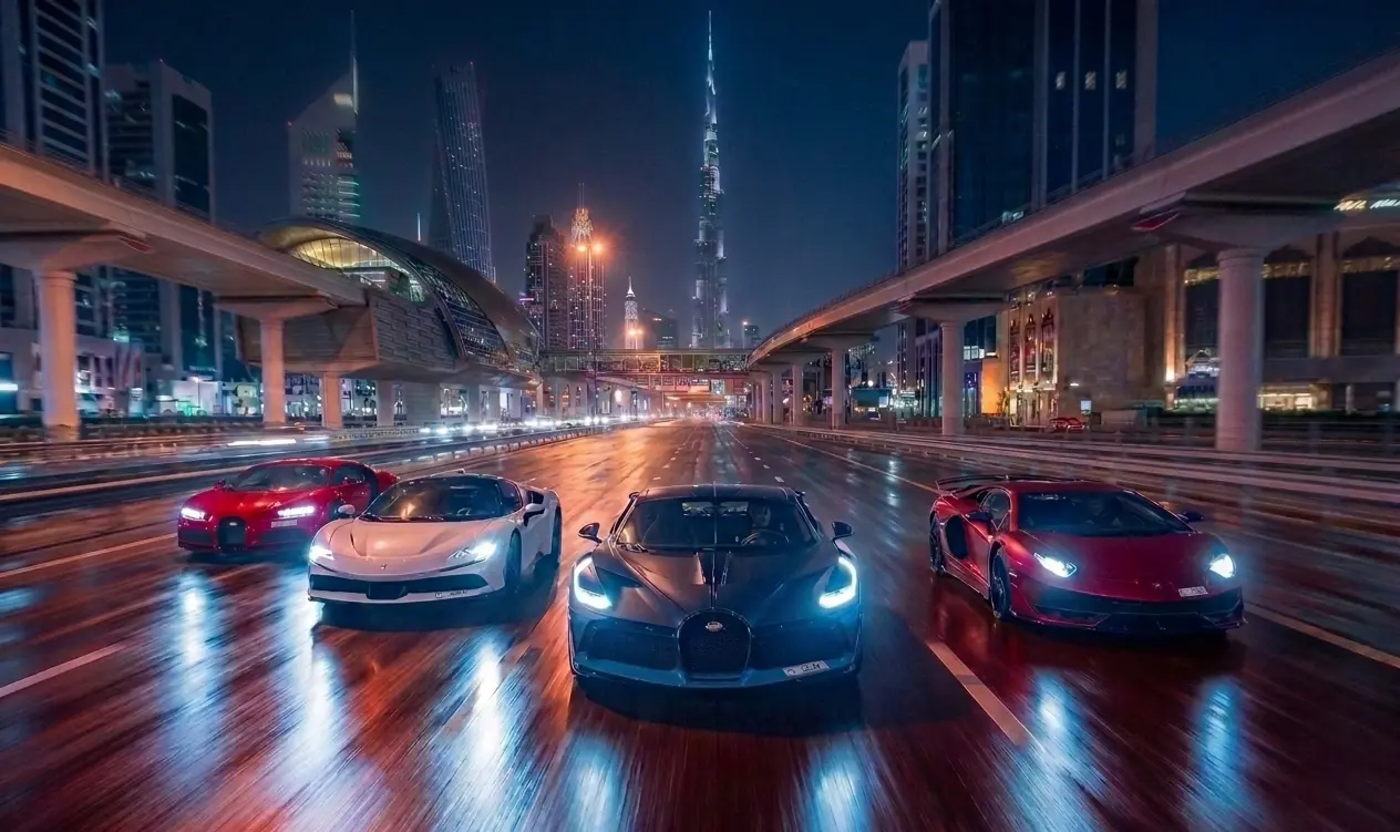 Four supercars driving at night on Sheikh Zayed Road with the Burj Khalifa lit behind them