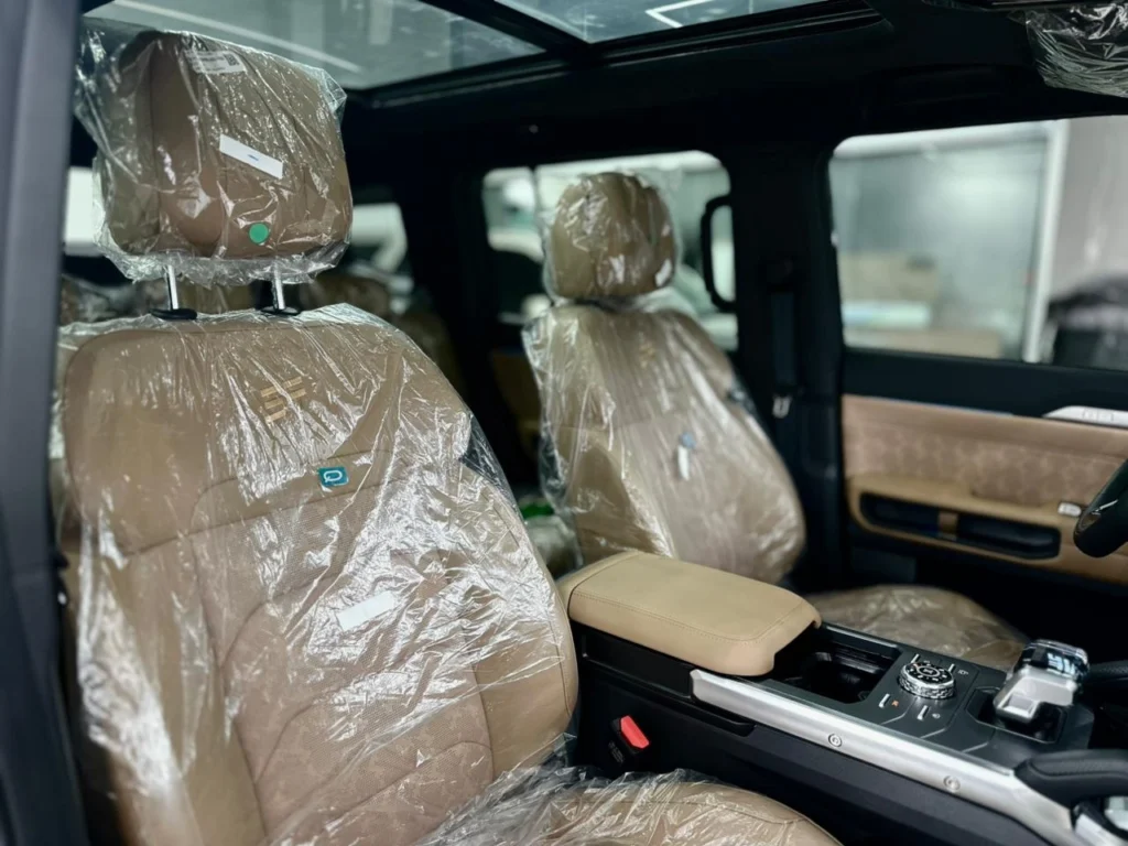 Beige leather front seats of the Jetour T2 2025, still under delivery plastic, with the panoramic glass roof above